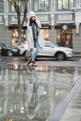 Young brunette woman walking around the city. She's wearing a gray coat and blue jeans
