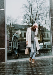 Young brunette woman walking around the city. She's wearing a gray coat and blue jeans