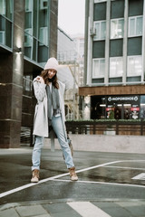 Young brunette woman walking around the city. She's wearing a gray coat and blue jeans