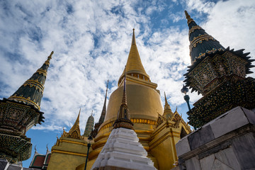 Fototapeta premium Grand Palace in Bangkok - looking up at temples and buildings against a partly cloudy sky