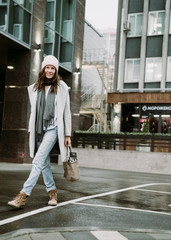 Young brunette woman walking around the city. She's wearing a gray coat and blue jeans