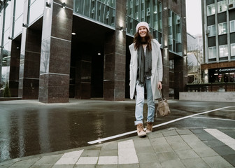 Young brunette woman walking around the city. She's wearing a gray coat and blue jeans