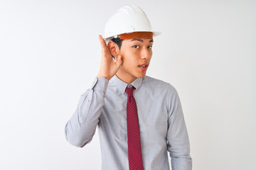 Chinese architect man wearing tie and helmet standing over isolated white background smiling with hand over ear listening an hearing to rumor or gossip. Deafness concept.