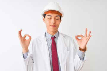 Chinese architect man wearing coat and helmet standing over isolated white background relax and smiling with eyes closed doing meditation gesture with fingers. Yoga concept.