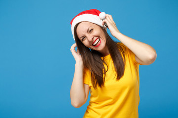 Laughing young woman Santa girl in yellow t-shirt Christmas hat posing isolated on blue background. Happy New Year 2020 celebration holiday concept. Mock up copy space. Listen music with headphones.