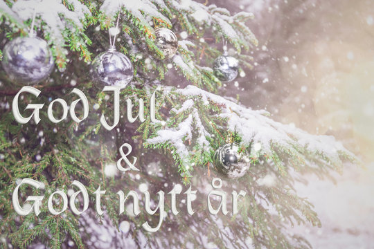 Text in Norwegian "God jul og Godt nytt ar"means "Merry Christmas and Happy New Year". Greetings in Norway. Blurred background of fir tree in snow decorated with silver lights, toys. Bokeh. Postcard.
