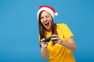 Crazy young woman Santa girl in Christmas hat posing isolated on blue wall background. Happy New Year 2020 celebration holiday concept. Mock up copy space. Hold joystick play game screaming, blinking.