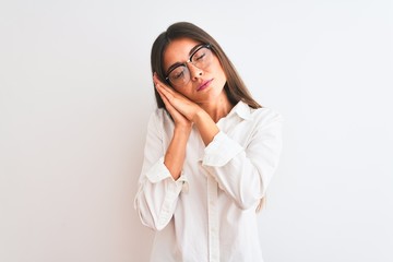 Young beautiful businesswoman wearing glasses standing over isolated white background sleeping tired dreaming and posing with hands together while smiling with closed eyes.