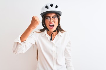 Beautiful businesswoman wearing glasses and bike helmet over isolated white background angry and mad raising fist frustrated and furious while shouting with anger. Rage and aggressive concept.