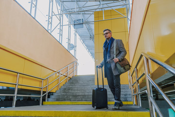 Naklejka na ściany i meble Elegant handsome gentleman holding travel suitcase at airport