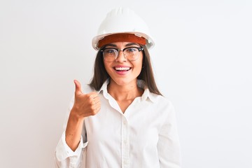 Young beautiful architect woman wearing helmet and glasses over isolated white background doing happy thumbs up gesture with hand. Approving expression looking at the camera showing success.