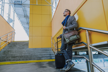 Fototapeta na wymiar Stylish young man with travel suitcase standing on stairs