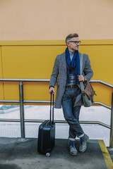 Fototapeta na wymiar Stylish young man holding handle of travel suitcase