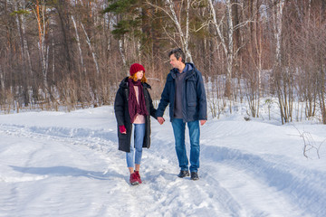 Fototapeta na wymiar Handsome man and attractive young woman walking along snowy country road in sunny day. Beautiful look, male and female fashion, winter outfit. Winter holidays, weekend at countryside concept