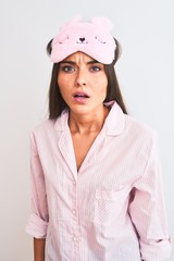 Young beautiful woman wearing sleep mask and pajama over isolated white background scared in shock with a surprise face, afraid and excited with fear expression