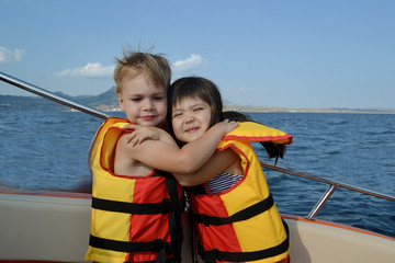Fototapeta na wymiar Little boy and girl in life jackets hugging on a boat in the open sea 