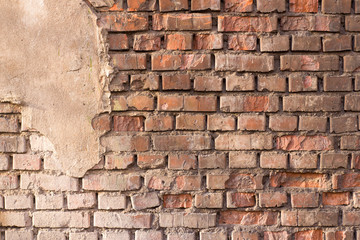 Background texture red old brick crumbling wall with a piece of crumbling plaster