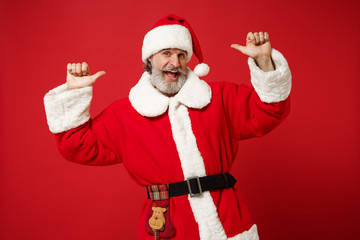 Fototapeta na wymiar Funny elderly gray-haired mustache bearded Santa man in Christmas hat posing isolated on red background. Happy New Year 2020 celebration holiday concept. Mock up copy space. Point thumbs on himself.