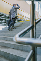 Elegant young man holding travel suitcase and climbing the stairs