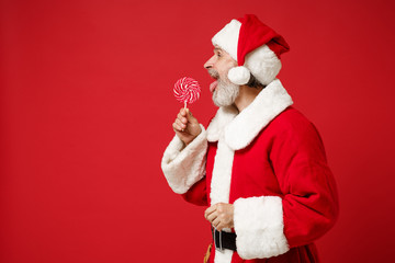 Side view of Elderly gray-haired mustache bearded Santa man in Christmas hat posing isolated on red...