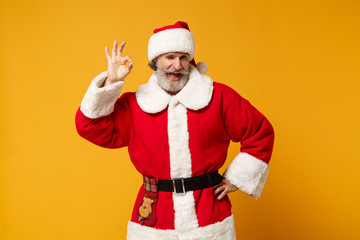 Fototapeta na wymiar Funny elderly gray-haired mustache bearded Santa man in Christmas hat posing isolated on yellow background. Happy New Year 2020 celebration holiday concept. Mock up copy space. Showing OK gesture.