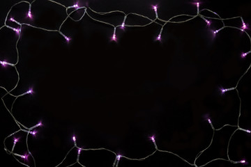 Christmas lights frame on black background. Holiday shiny purple garland border top view. Winter holidays illumination.