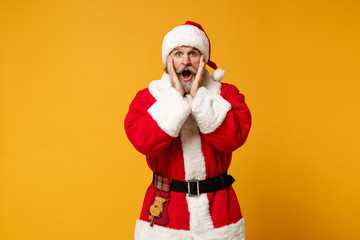 Fototapeta na wymiar Shocked elderly gray-haired mustache bearded Santa man in Christmas hat posing isolated on yellow background. New Year 2020 celebration holiday concept. Mock up copy space. Putting hands on cheeks.