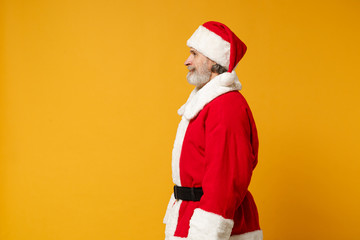 Fototapeta na wymiar Side view of elderly gray-haired mustache bearded Santa man in Christmas hat posing isolated on yellow background studio portrait. Happy New Year 2020 celebration holiday concept. Mock up copy space.