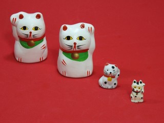 Four little Maneki Neko, Japanese lucky cats, amulets that bring good luck, protection, prosperity, health and happiness. They look like a family: father, mother and sons. Red background.