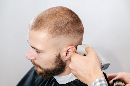 Barber shaves the bearded client's head with electric trimmer
