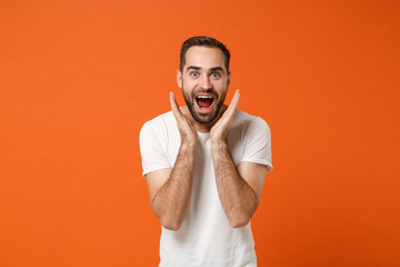 Excited young man in casual white t-shirt posing isolated on bright orange wall background, studio...