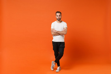 Fototapeta na wymiar Handsome attractive young man in casual white t-shirt posing isolated on orange wall background studio portrait. People sincere emotions lifestyle concept. Mock up copy space. Holding hands crossed.