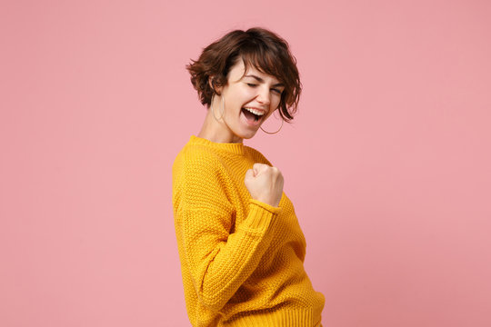 Side view of young brunette woman girl in yellow sweater posing isolated on pastel pink background studio portrait. People sincere emotions lifestyle concept. Mock up copy space. Doing winner gesture.
