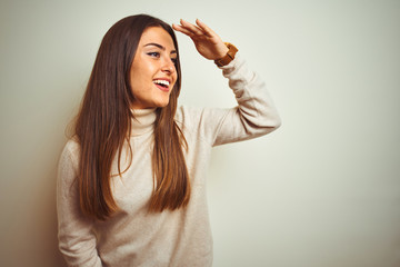 Young beautiful woman wearing winter turtleneck sweater over isolated white background very happy and smiling looking far away with hand over head. Searching concept.