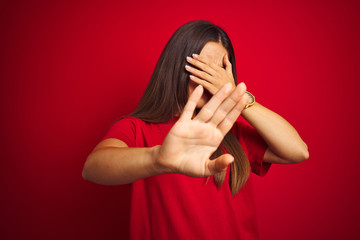 Young beautiful woman wearing t-shirt standing over isolated red background covering eyes with hands and doing stop gesture with sad and fear expression. Embarrassed and negative concept.