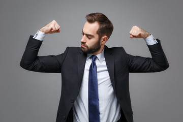 Strong young business man in classic black suit shirt tie posing isolated on grey background studio portrait. Achievement career wealth business concept. Mock up copy space. Showing biceps, muscles.