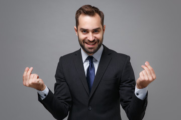Smiling business man in classic suit shirt tie posing isolated on grey background. Achievement career wealth business concept. Mock up copy space. Rubbing fingers showing cash gesture ask for money.
