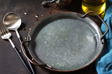 Culinary background. Round wooden metal plate, cutlery with herbs and spices around on a dark stone background.