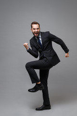 Fototapeta na wymiar Overjoyed young business man in classic black suit shirt tie posing isolated on grey background. Achievement career wealth business concept. Mock up copy space. Clenching fists like winner, screaming.