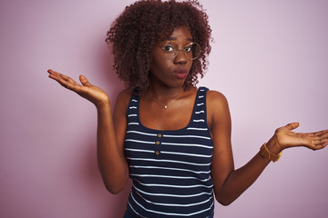Young african afro woman wearing striped t-shirt glasses over isolated pink background clueless and...