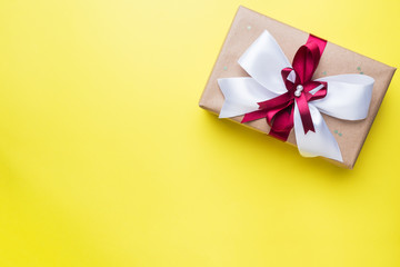 Gift or present box with a big bow on a yellow table top view. Flatlay composition for Christmas birthday, mother day or wedding.