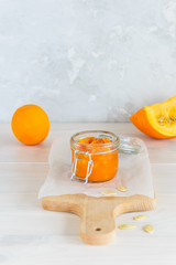 Pumpkin jam with orange in a jar on a wooden board.