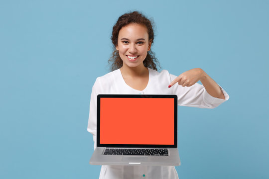 African american doctor woman isolated on blue background. Doctor in medical gown point finger on laptop pc computer with blank empty screen. Healthcare personnel medicine concept. Mock up copy space.