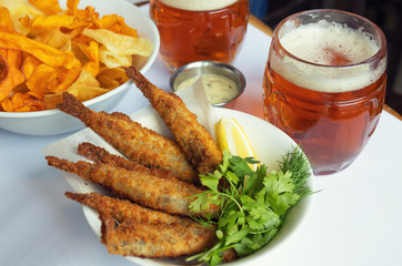 Mug with beer and beer snacks. Fried fish with chips and sauce.