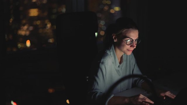 Successful female professional completing task during evening deadline work in office interior, Caucasian woman in classic spectacles for provide eyes protection reading web news