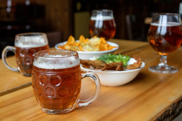 Mug with beer and beer snacks. Corn chips with sauce, fish and greens.
