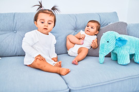 Beautiful infant happy girls playing together at home kindergarten sitting on the sofa