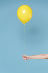 Close up cropped photo of female hold in hands yellow air balloon isolated on blue wall background in studio. Copy space advertising mock up. Birthday holiday party, people emotions concept.