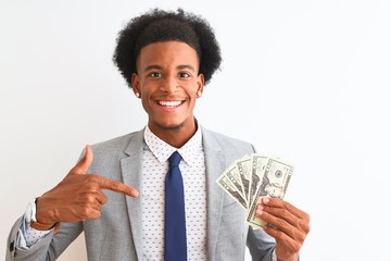 Young african american businessman holding dollars standing over isolated white background with surprise face pointing finger to himself