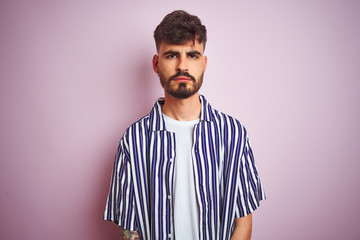 Young man with tattoo wearing striped shirt standing over isolated pink background skeptic and nervous, frowning upset because of problem. Negative person.